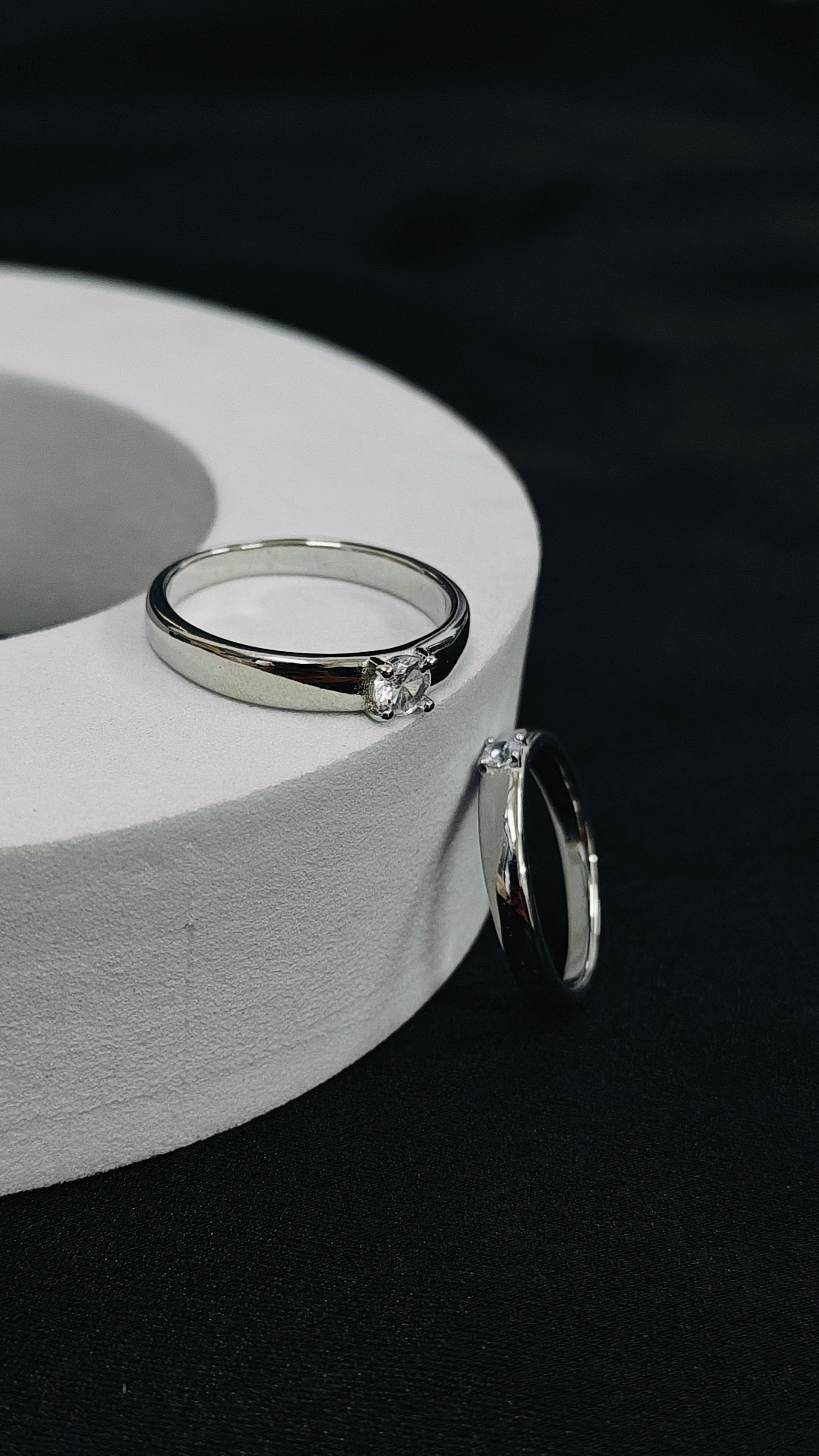 Silver ring with a diamond on a white cylindrical stand against a black background